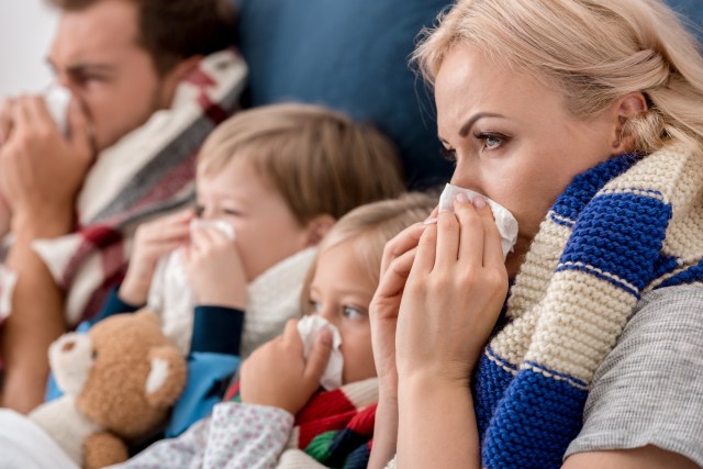 close-up shot of sick young family blowing noses with napkins together while lying in bed